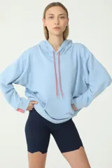 Buzo hoodie celeste de rústico, con capucha y cordones de ajuste color salmón y verde. Tiene etiqueta de la marca en la manga derecha con logo Basset 00'S.