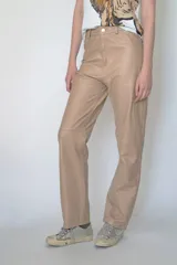 Pantalón de cuero color beige, de corte recto y tiro alto. Presenta bolsillos delanteros y traseros, y trabillas para cinturón.