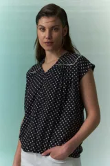 Blusa negra con lunares blancos, escote en V y cuello bebé con borde blanco.