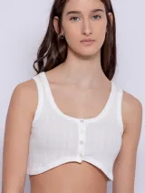 Top blanco de tela texturada, sin mangas y con cuello redondo. Cuenta con cuatro botones y terminación en curva en la parte delantera.