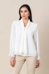 Blusa blanca de gasa italiana con cuello plisado cayendo sobre la blusa y mangas amplias terminando en un volado.