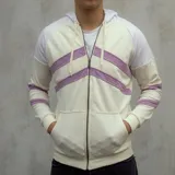 Campera con capucha de algodón color crema con mangas y capucha blancas. Presenta cierre frontal y bolsillos tipo canguro. Tiene dos franjas diagonales color lila en el pecho y una franja lila en cada puño.