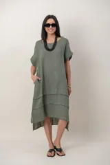 Vestido midi de lino color beige, de corte holgado y silueta acampanada. Cuenta con cuello redondo, mangas cortas amplias, bolsillos laterales y detalles de recortes horizontales en la falda con terminación asimétrica más larga en la parte trasera.