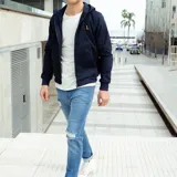 Campera azul marino de gabardina con capucha, cierre frontal con cremallera, puños y cintura acanalados y un pequeño logo bordado en el pecho.