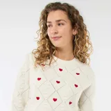 Sweater de punto color blanco con diseño de rombos en relieve y pequeños corazones rojos bordados. Presenta cuello redondo y puños acanalados.