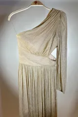Vestido largo de fiesta color dorado con textura plisada, corte asimétrico con un solo hombro y manga larga abullonada. Presenta abertura lateral en la cintura y falda con caída fluida.
