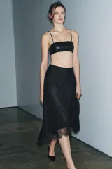 Falda midi negra de tiro medio, confeccionada en tejido de encaje con forro interior a tono. Presenta un bajo asimétrico con terminación en línea evasé y cierre lateral oculto.