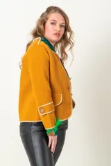 Chaqueta mostaza de tejido plano con vivos blancos, corte clásico y cierre frontal con botones dorados.