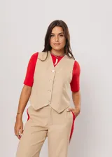 Chaleco beige con escote en V, sin mangas y cierre frontal con botones. Presenta pespuntes en color rojo y logo bordado en la espalda.