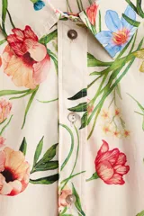 Vestido midi de corte camisero con estampado floral multicolor sobre base beige, cuello camisero, botonadura frontal completa, mangas cortas con lazo y cinturón del mismo género para ajustar en la cintura.