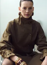 Chaqueta de gabardina color verde militar, de corte oversize con cuello alto abotonado de manera asimétrica, mangas largas con puños ajustables y cinturón ajustable del mismo tejido.