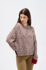 Sweater de tejido de punto con efecto jaspeado, corte holgado y cuello redondo. Presenta mangas largas con puños en contraste de color, uno en tono oscuro y otro en tono rojizo.