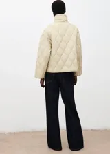 Campera acolchada de diseño oversize en color beige, con cuello alto, cierre frontal de cremallera y botones, y bolsillos laterales.