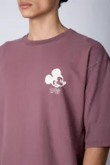 Remera negra de corte oversize confeccionada en algodón pesado, con estampa pequeña de Mickey Mouse en el pecho y diseño gráfico en la espalda.