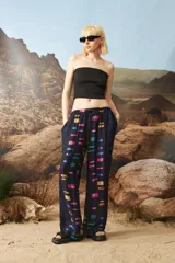 Pantalón de corte holgado y tiro medio, con cintura elástica y cordón de ajuste. Presenta un estampado geométrico multicolor sobre fondo negro.