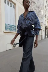 Camisa de rayas verticales azules y blancas, de cuello solapa con escote en V y cierre frontal con botones. Presenta mangas abullonadas por debajo del codo.