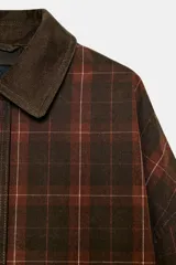 Chaqueta de mujer de la colección Zara Woman, confeccionada en algodón 100% con acabado encerado. Presenta un estampado a cuadros en tonos marrón y rojo, cuello solapa de pana, manga larga con puño y botón, bolsillos de plastrón con solapa en el delantero y cierre frontal con botones a presión.