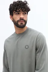 Remera de manga larga color blanco roto o gris muy claro, con escote redondo y un pequeño logo circular estampado en el pecho.