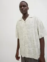Camisa de manga corta con cuello resort y corte amplio. Confeccionada en tejido plano con estampado geométrico y botánico en tonos neutros.