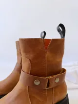 Bota de cuero color marrón con suela de goma negra, cierre lateral y pulsera desmontable con hebilla.