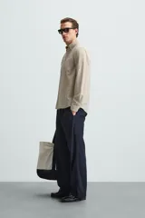 Camisa celeste a rayas verticales, de corte relaxed fit, confeccionada en lino y algodón. Tiene cuello abotonado, manga larga con puños abotonados, bolsillo de parche en el pecho y cierre frontal con botones.