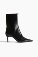Botines de caña media con acabado brillante, punta fina y taco fino revestido. Presentan cierre lateral y diseño minimalista.