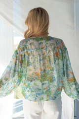 Blusa estampada en tonos de verde, celeste y amarillo, con sutiles hilos de lurex dorados. Cuello con lazo y abotonadura, y corte en el pecho con fruncido.