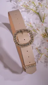 Cinturón beige con hebilla ovalada dorada con strass y detalle de strass en el extremo.