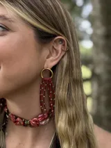 Aros colgantes con base circular dorada y flecos de tiento color borgoña con cuentas metálicas doradas.