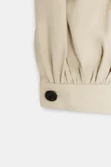 Pantalón de tiro alto en color beige, con diseño de pierna holgada y puños elásticos con cierre de botón en el bajo. Presenta cierre frontal con cremallera y doble botón en la cintura, además de bolsillos laterales.