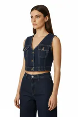 Chaleco corto de denim azul oscuro, estilo vaquero, con cuello en V, cierre frontal de botones y dos bolsillos de parche con tapa en el pecho.