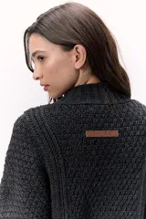 Sweater de lana merino tejido en punto grueso, color gris oscuro, con cuello alto. Presenta un diseño calado con tientos de cuero marrón insertados a lo largo de la prenda, simulando un lazo o detalle orgánico.