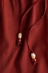 Pantalón de pierna recta en tejido liviano mezcla de lino y viscosa, color rojo. Cuenta con cintura elástica de tiro bajo, cordón de ajuste con cuentas decorativas en los extremos y bolsillos laterales al bies.