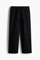 Jogger de punto de algodón color negro, con cintura elástica y cordón de ajuste, bolsillos laterales y pliegues frontales pespunteados. Corte relajado de pernera recta.