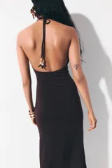 Vestido midi de punto color marrón, con diseño halter, escote pronunciado y frunces laterales que generan un efecto drapeado. Cuenta con cordón ajustable en la nuca adornado con cuentas en los extremos.