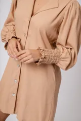 Vestido corto color tostado, con cuello solapa, abotonado al frente y mangas 3/4 con puños fruncidos.