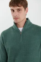 Sweater verde de punto inglés con cuello alto y cierre metálico frontal. Tiene mangas largas y terminaciones en punto canalé.