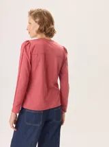 Remera de manga larga color rosado con cuello en V. Presenta detalles de costuras verticales tipo alforzas en el frente y hombros ligeramente fruncidos.