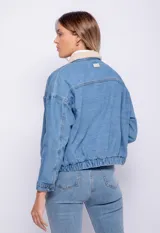 Campera de jean celeste con cuello y forro de corderito color crema, corte cuadrado, cierre frontal con botones metálicos, dos bolsillos de parche en el pecho y elástico en el ruedo.