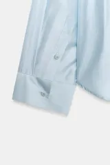 Camisa amplia de cuello solapa con escote en pico y manga larga, en tejido satinado de color bordó. Cuenta con un bolsillo de plastrón en el frente y un diseño holgado.