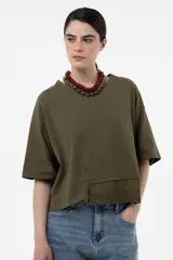Remera verde militar de calce relajado y silueta amplia, con mangas cortas, hombros caídos y largo levemente cropped. Presenta una terminación de broderie en el frente.