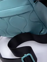 Bandolera rectangular color celeste, confeccionada en nylon reciclado con capitoneado ondulado. Cuenta con un bolsillo externo, uno interno y una correa regulable negra.