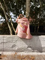 Campera con capucha de textura tipo corderito en color rosa, con diseño de collage en la espalda que combina diferentes texturas y tonos de rosa con detalles en dorado.