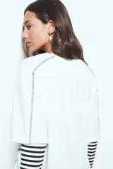 Remera de manga corta con silueta relajada y costuras a la vista en color blanco que contrastan sobre el tejido negro. Presenta un diseño moderno con terminaciones destacadas.