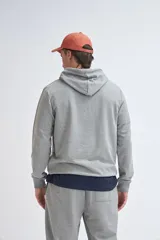Hoodie deportivo de color gris melange, con capucha y mangas largas. Presenta un diseño básico y versátil, ideal para actividades deportivas o uso diario.