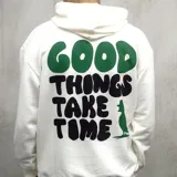 Canguro blanco con capucha, cordones ajustables y bolsillo tipo canguro. Estampado frontal con la frase "Good things take time" en verde y azul.