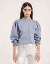 Blusa celeste de cuello mao y mangas abullonadas con puños elásticos. Tiene tajos laterales y botones en la delantera.