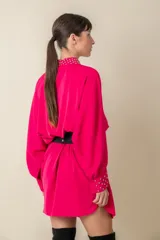 Camisa larga negra con tachas plateadas en cuello y puños, manga dolman con puño importante y botones forrados.