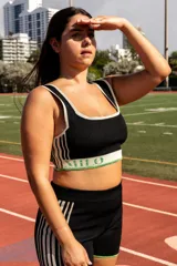 Top deportivo negro tejido con hilados reciclados, con cuello cuadrado, tirantes anchos y banda inferior con logo en verde y blanco.