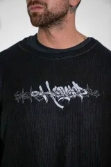 Buzo de tejido de punto fino en color negro, con diseño de cuello redondo y corte holgado. Presenta un estampado gráfico estilo gótico en el centro del pecho.